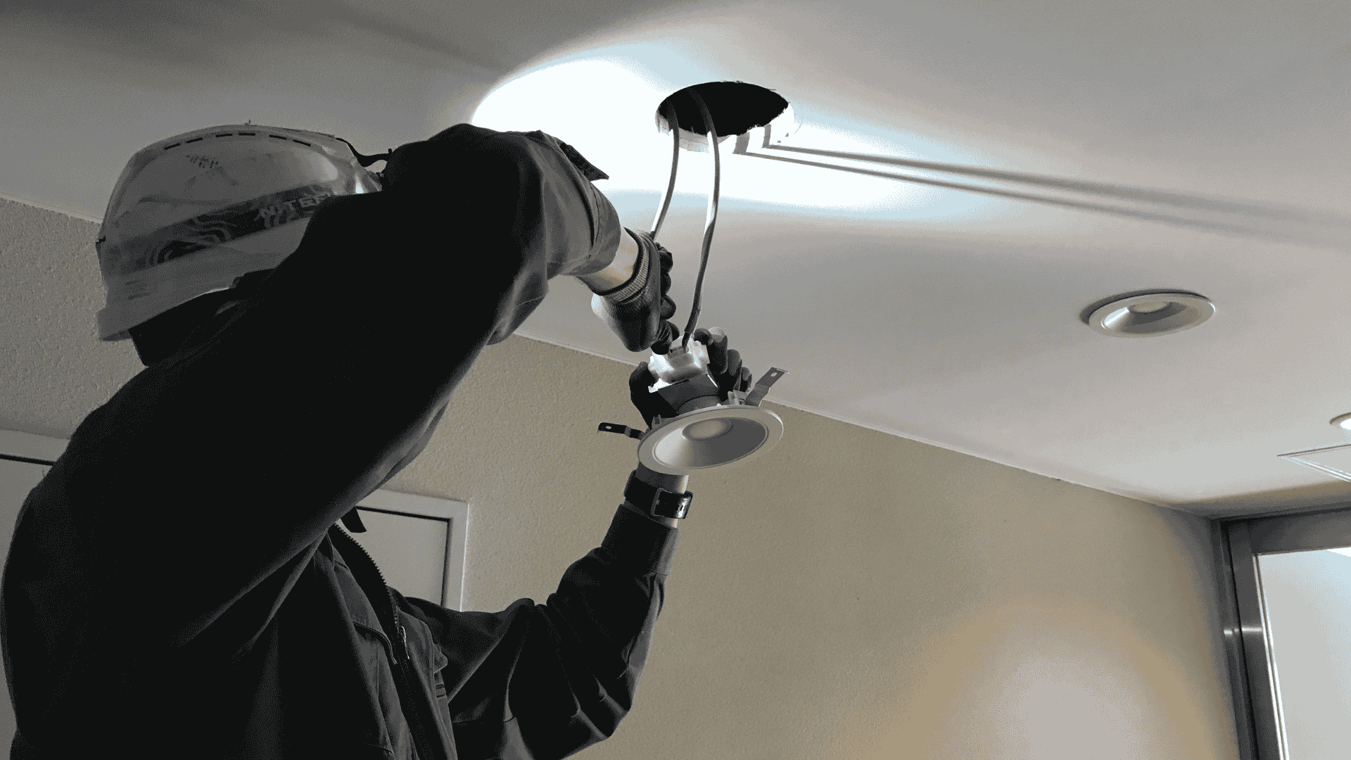 Electrician repairing recessed ceiling lighting fixture inside residential property